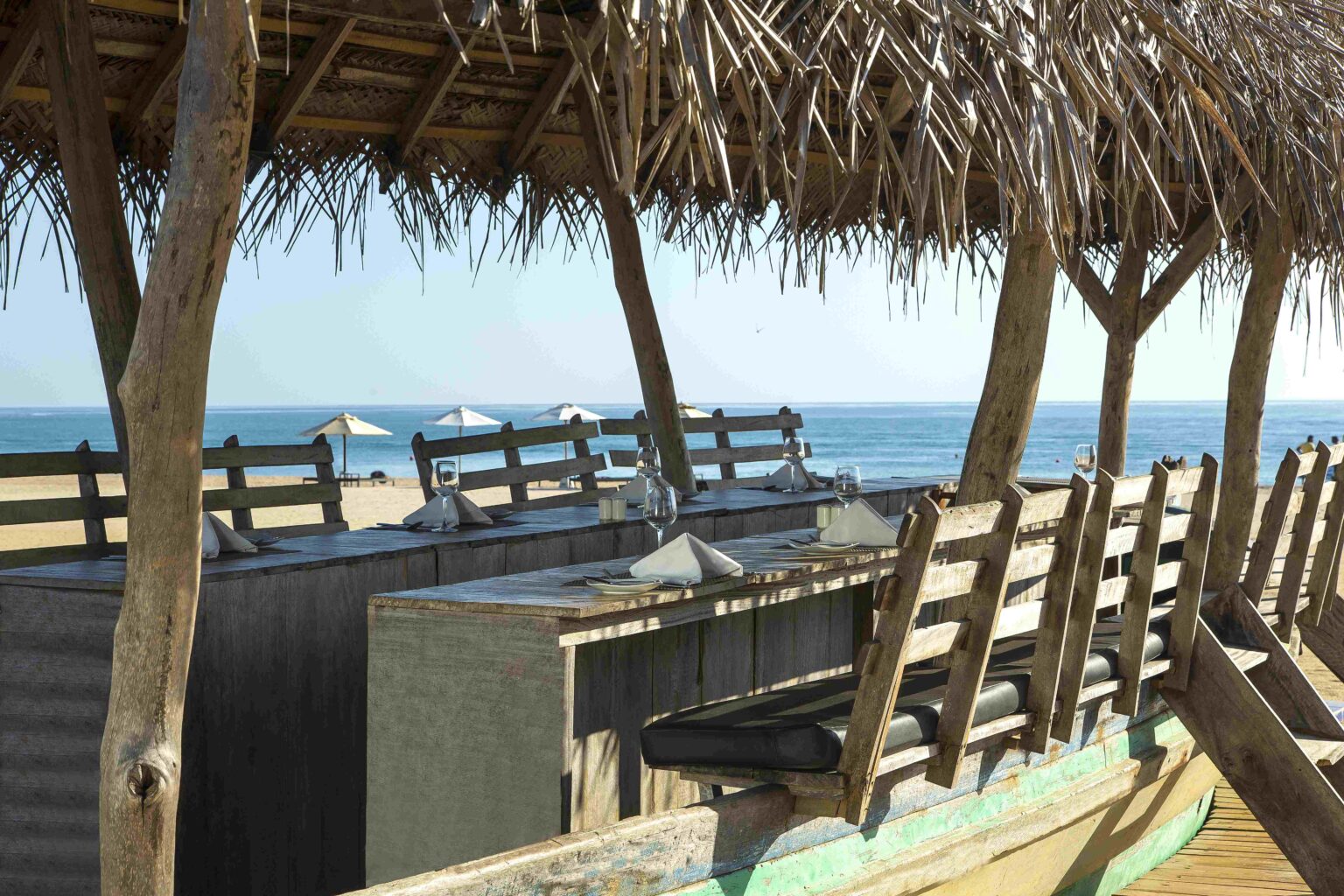 Tables under a thatched roof beside the beach, looking out to sea