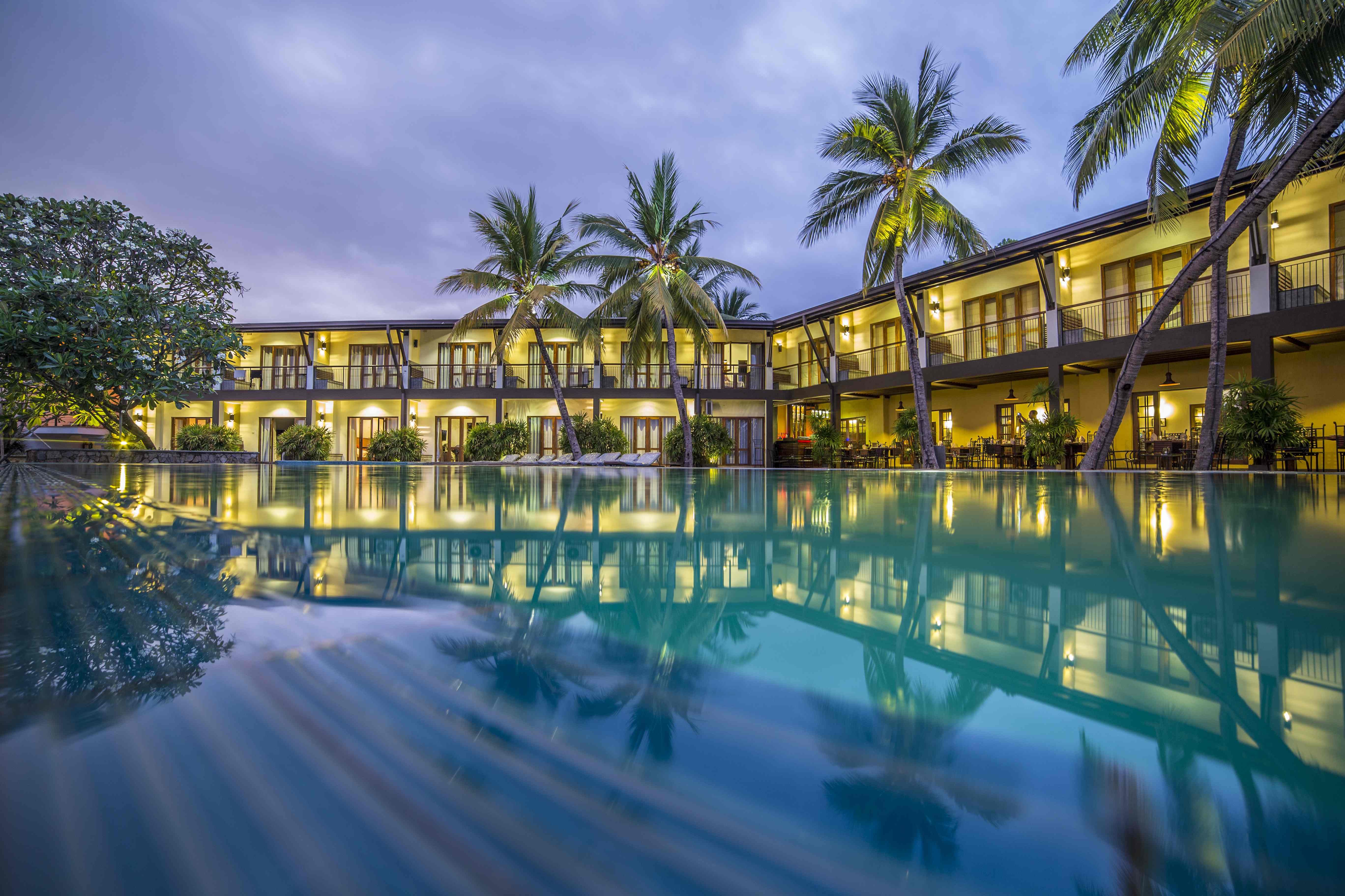 Tranquil evening at a Sri Lanka Yala National Park hotel with palm trees, glowing lights, and a serene infinity pool.