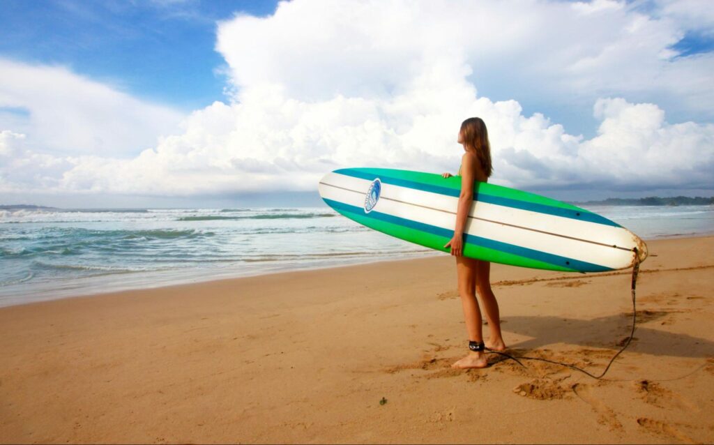 Surfer standing on a sandy beach in Weligama preparing for a surf session