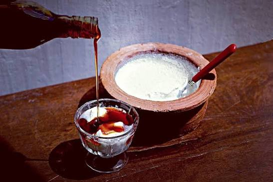 Treacle being poured over buffalo curd beside a clay pot of curd