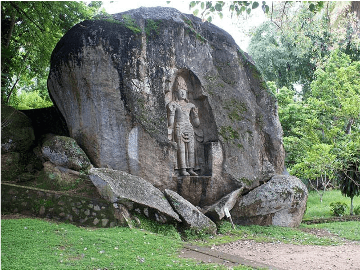 Moss-covered boulder and shaded grove of trees surrounding the Kushtarajagala carving, Weligama