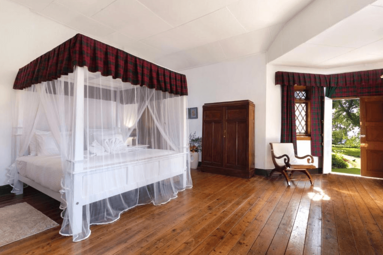 A four-poster bed on wooden floors in a guest room at Scottish Planter Bungalow, with a door opening onto the garden.