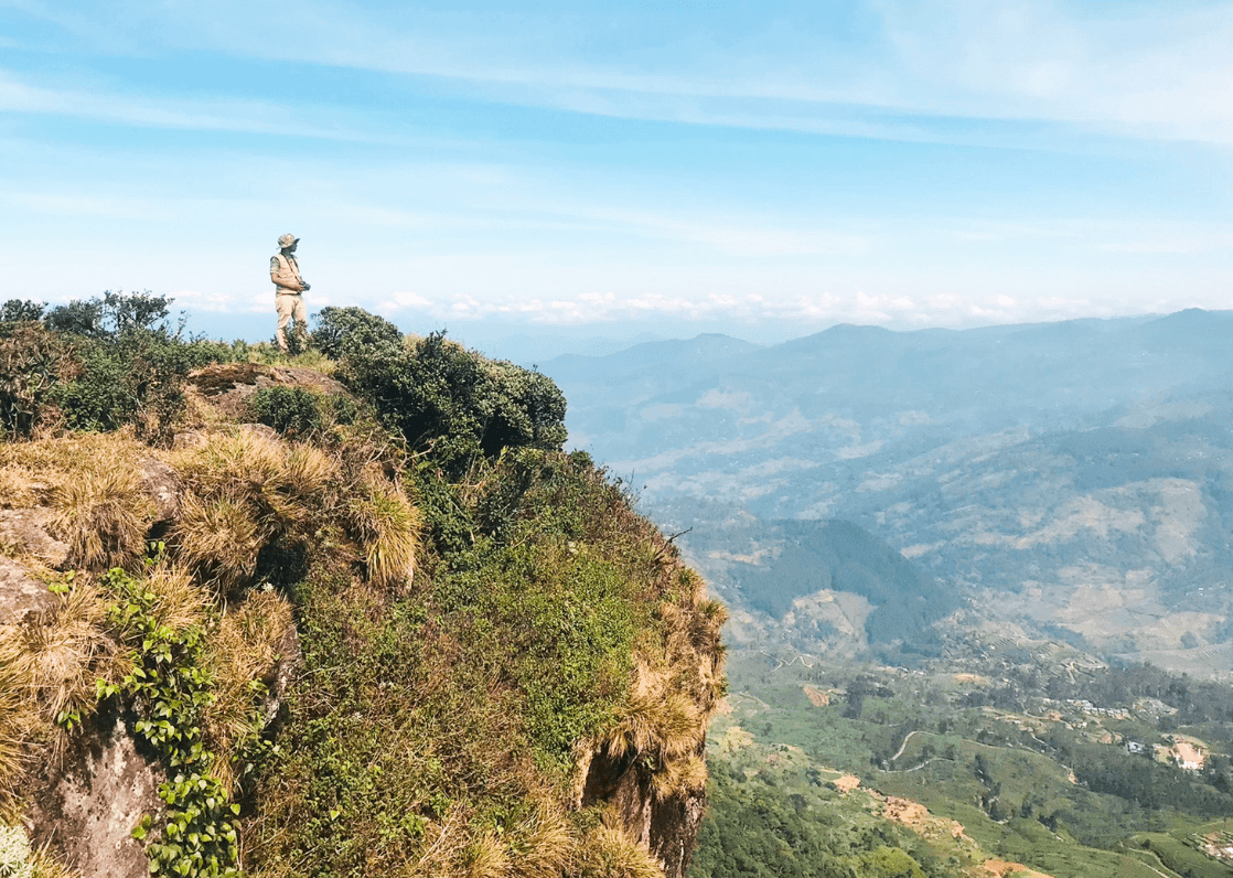 Trekker at the summit of Kabaragalla Mountain with panoramic hill country views.