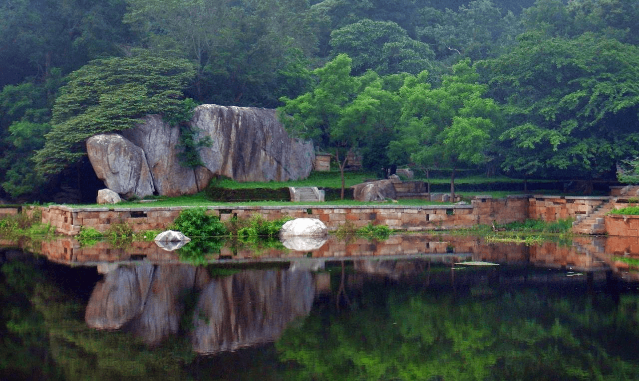 Stone ruins and a moat among trees at the Kaludiya Pokuna monastery site near Kandalama